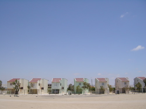A row of identical pastel-painted two-storey beach houses lined up on a sandy plain in Bahía Inglesa under a cloudless deep-blue Pacific sky.