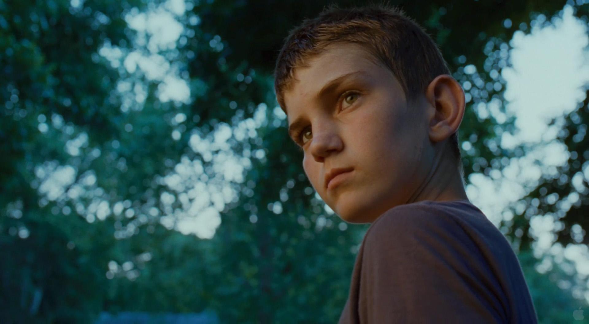 Hunter McCracken as the young Jack, in close-up against soft greenery, light catching one side of his face. From The Tree of Life, Terrence Malick, 2011.